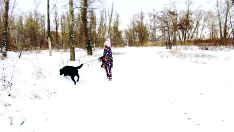 Kleines-Mädchen-spielt-mit-ihren-schwarzen-Labrador-auf-Schnee