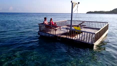 v03847-vuelo-drone-vista-aérea-de-Maldivas-playa-2-personas-pareja-hombre-mujer-relajante-en-la-isla-de-paraíso-tropical-soleado-con-cielo-azul-aqua-agua-mar-4k-flotante-pontoon-embarcadero-el-sol-juntos