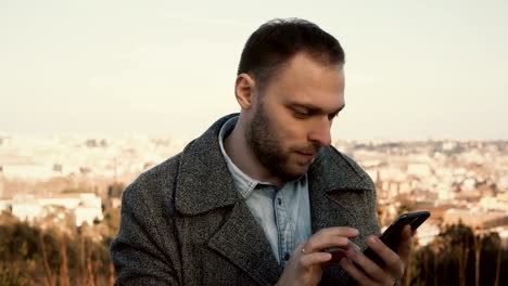 Portrait-of-young-handsome-man-standing-at-the-panorama-of-Rome,-Italy.-Male-use-the-smartphone-outside