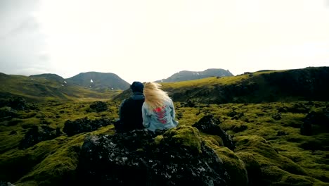 Rückansicht-des-jungen-schönen-Paar-auf-dem-Felsen-sitzen-und-genießen-Sie-die-malerische-Landschaft-des-die-Lavafelder-in-Island