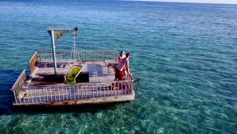 v03856-fliegenden-Drohne-Luftaufnahme-der-Malediven-weißen-Sandstrand-2-Personen-junges-Paar-Mann-Frau-entspannend-auf-sonnigen-tropischen-Inselparadies-mit-Aqua-blau-Himmel-Meer-Wasser-Ozean-4k-schwimmenden-Ponton-Steg-Sonnenbaden-zusammen