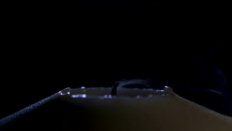 Slow-motion-macro-footage-of-a-white-candle-lit-by-a-match-on-a-dark-background