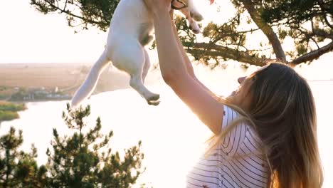 Young-attractive-woman-playing-with-a-dog-Jack-Russell-in-the-meadow-at-sunset-with-sea-background.-slow-motion