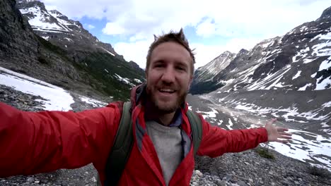 Young-cheerful-man-hiking-on-glacier-takes-selfie-portrait