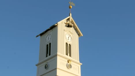 Spitze-des-Turms-der-isländischen-Kirche-mit-Uhr,-Glocken-und-Wetterhahn,-gegen-blauen-Himmel