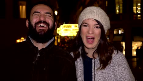 smiling-couple-laughing-in-street-at-winter-night,looking-camera-slow-motion