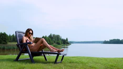 Beautiful-brunette-in-a-swimsuit-lying-on-a-sun-lounger-on-the-lake-smiling-working-remotely-via-the-Internet-in-the-business-sphere.-The-concept-of-country-life