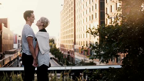 Beautiful-Hispanic-man-and-Caucasian-woman-stand-holding-hands,-looking-at-each-other-on-New-York-City-sunset-bridge