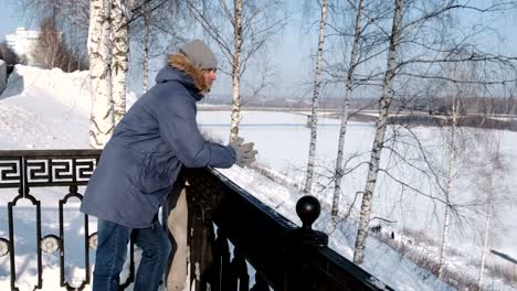 Hombre-en-azul-por-la-chaqueta-con-piel-campana-está-parado-en-la-valla-y-mire-a-su-alrededor-en-el-parque-de-invierno.