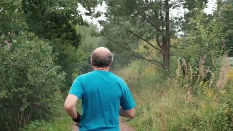 Mature-man-running-on-road-through-trees.-Back-view.