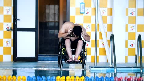 Disabled-man-in-a-wheelchair-putting-on-a-swimming-cap-and-a-goggles.-Front-angle