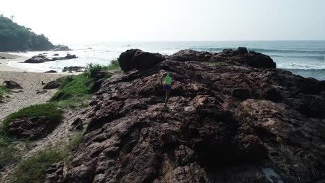 Young-woman-open-arms-on-cliff-edge-at-seaside,aerial-footage