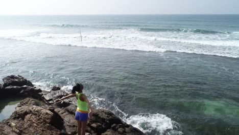 Young-woman-open-arms-on-cliff-edge-at-seaside,aerial-drone-4k-footage