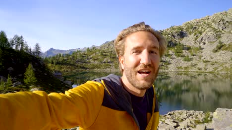 Young-man-taking-selfie-at-mountain-lake.-Man-hiking-in-Switzerland-takes-selfies-surrounded-by-stunning-mountain-landscape.-Selfie-travel-adventure-lifestyle