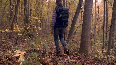 Man-with-a-ponytail-wearing-a-backpack-walking-in-the-woods-away-from-the-camera