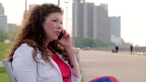 Woman-sits-listening-to-phone-on-bench-by-Detroit-River