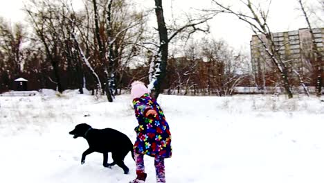 Kleines-Mädchen-spielt-mit-ihren-schwarzen-Labrador-auf-Schnee