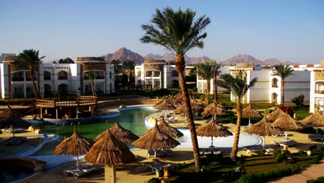 Sunny-Hotel-Resort-with-Blue-Pool,-Palm-Trees-and-Sunbeds-in-Egypt