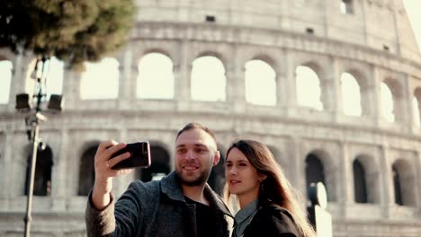 Joven-pareja-feliz-viajando-en-Roma,-Italia.-Hombre-y-la-mujer-tomando-la-foto-selfie-en-smartphone-cerca-del-Coliseo