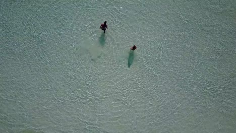 v03808-Aerial-flying-drone-view-of-Maldives-white-sandy-beach-on-sunny-tropical-paradise-island-with-aqua-blue-sky-sea-water-ocean-4k-2-people-young-couple-man-woman-playing-ball-fun-together