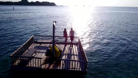 v03854-vuelo-drone-vista-aérea-de-Maldivas-playa-2-personas-pareja-hombre-mujer-relajante-en-la-isla-de-paraíso-tropical-soleado-con-cielo-azul-aqua-agua-mar-4k-flotante-pontoon-embarcadero-el-sol-juntos