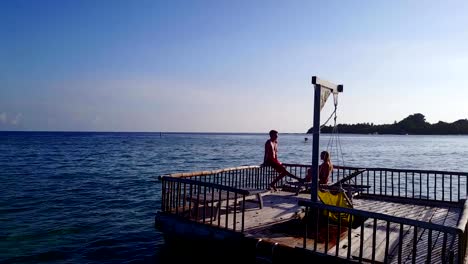 v03827-vuelo-drone-vista-aérea-de-Maldivas-playa-2-personas-pareja-hombre-mujer-relajante-en-la-isla-de-paraíso-tropical-soleado-con-cielo-azul-aqua-agua-mar-4k-flotante-pontoon-embarcadero-el-sol-juntos