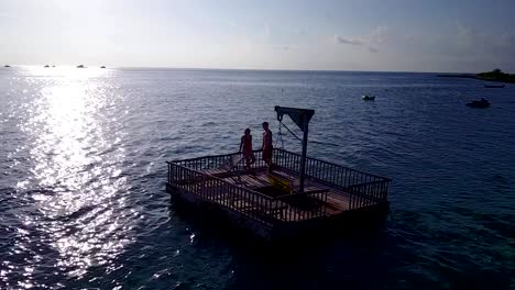 v03842-vuelo-drone-vista-aérea-de-Maldivas-playa-2-personas-pareja-hombre-mujer-relajante-en-la-isla-de-paraíso-tropical-soleado-con-cielo-azul-aqua-agua-mar-4k-flotante-pontoon-embarcadero-el-sol-juntos