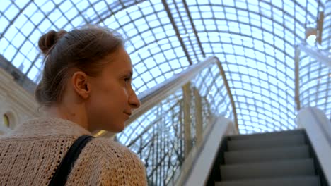 Young-woman-moving-on-escalator-and-looking-around-in-mall