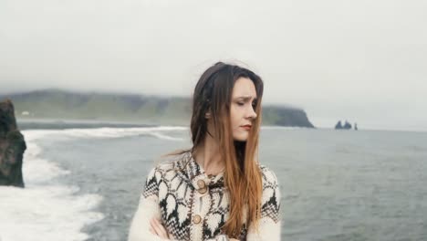 Young-beautiful-woman-standing-on-the-black-beach,-near-the-Troll-toes-in-Iceland-and-looking-around-in-windy-day