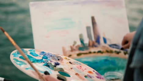 Closeup-view-of-female-hand-with-brush-and-palette-painting-the-picture-on-the-shore-of-Michigan-lake,-Chicago,-America