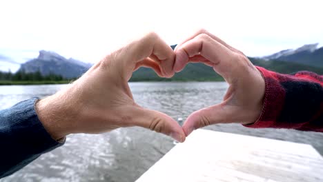 Close-up-on-hands-making-heart-shape-frame-on-mountain-lake-landscape