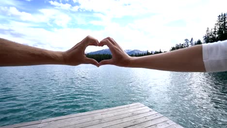 Close-up-on-hands-making-heart-shape-frame-on-mountain-lake-landscape