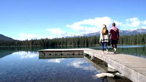 Young-couple-having-a-walk-over-wooden-pier-above-stunning-mountain-lake-scenery