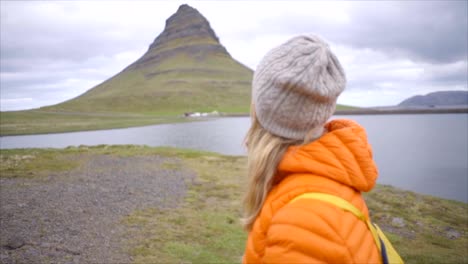 Mujer-joven-en-Islandia-contemplando-la-famosa-montaña-de-Kirkjufell,-reflexión-sobre-fiordo