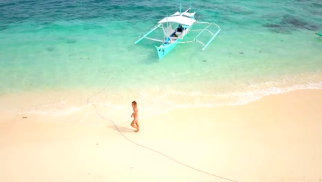 Drone-shot-aerial-view-of-young-woman-walking-on-idyllic-tropical-beach