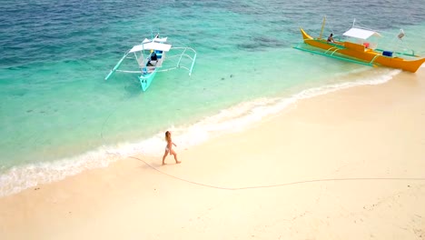 Drone-shot-aerial-view-of-young-woman-walking-on-idyllic-tropical-beach