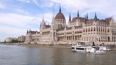 El-paisaje-del-edificio-del-Parlamento-húngaro-con-consejos-de-la-nave-en-el-Danubio-en-Budapest,-Hungría-en-la-tarde.