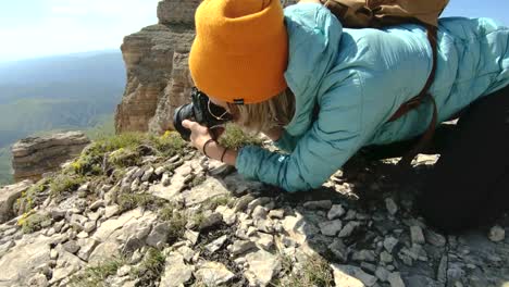 Un-fotógrafo-de-la-chica-rubia-en-un-sombrero-toma-una-foto-en-una-pose-extraña-en-su-cámara-digital-con-un-fondo-de-rocas-en-el-Cáucaso