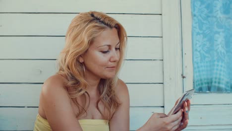 Blonde-woman-typing-message-by-mobile-phone-and-resting-on-summer-terrace