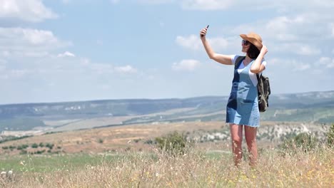 Active-woman-tourist-with-backpack-taking-selfie-in-the-field-using-smartphone