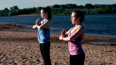 Dos-mujer-estiramiento-permanente-de-yoga-en-la-playa-por-el-río-en-la-ciudad.-Vista-hermosa-ciudad.-Pose-de-Namaste.