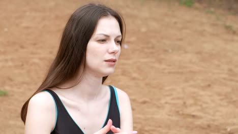 Young-beautiful-brunette-woman-talking-to-someone-sitting-on-the-sand-on-the-beach.