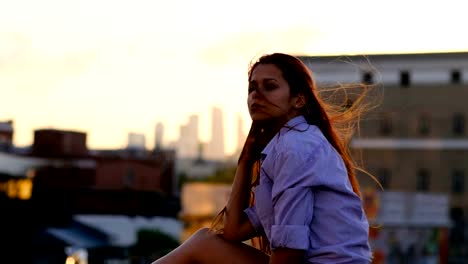 Hermosa-mujer-con-pelo-largo-rojo-en-la-azotea.-Puesta-de-sol-de-luz,-viento