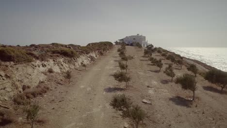 Vista-aérea-de-una-carretera-de-tierra-con-una-casa-grande-en-el-mar,-Grecia.