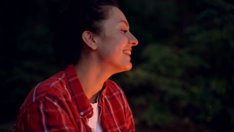 Close-up-portrait-of-attractive-young-woman-tourist-sitting-near-campfire-and-singing-songs-enjoying-nature-and-music.-People,-forest-and-relaxation-concept.