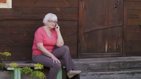 Talking-on-phone-while-sitting-on-bench-near-wooden-house-on-countryside