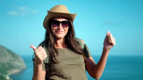 Portrait-of-woman-hiker-in-hat-and-sunglasses-enjoying-sun-raising-hands-getting-big-thumbs-up