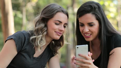 Authentic-friends-together-outdoors-checking-cellphone.-Girls-looking-and-holding-smartphone-chatting-exchanging-gossip