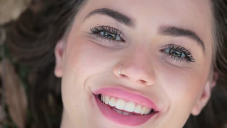 Pretty-girl-opens-eye-while-laying-down-on-grass-at-the-park.-Woman-with-green-eyes-opening-eyes-looking-to-camera