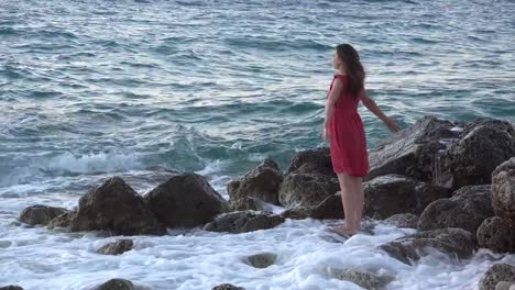 Beautiful-young-woman-on-rocky-seashore-open-arms-in-the-wind,-waves-splash